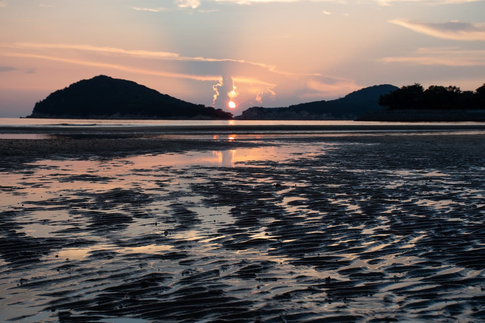 The sun setting between two hills behind a wet tidal flat